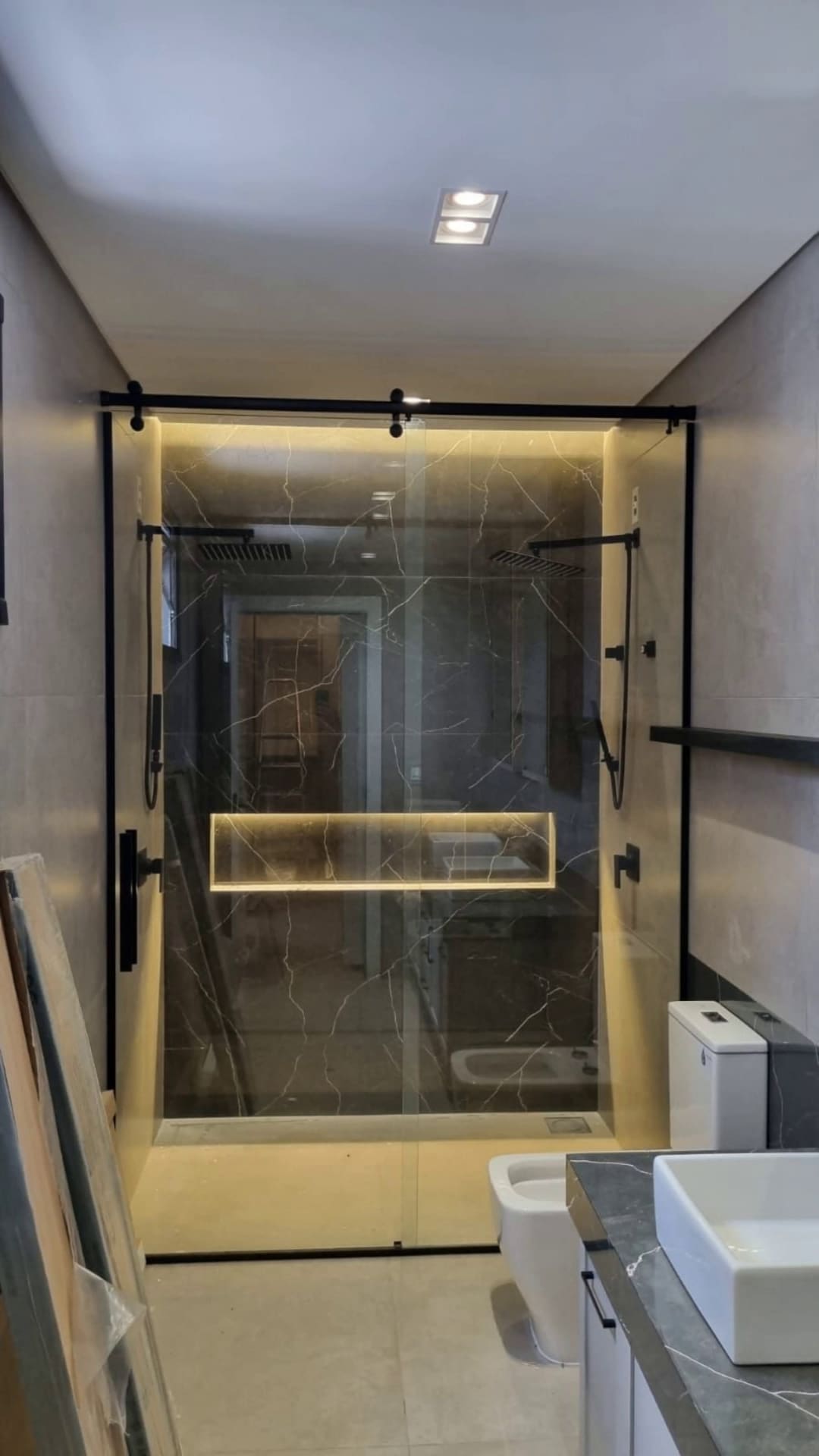 Box de vidro com iluminação LED em banheiro de mármore escuro